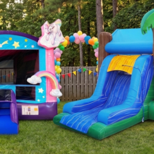 A photo of two backyard inflatable bounce houses side-by-side on green grass at a house party, featuring a magical unicorn-themed bounce house with stars and rainbows and a large tropical bouncer with a blue slide and palm trees. A party flag banner is on a fence behind them.