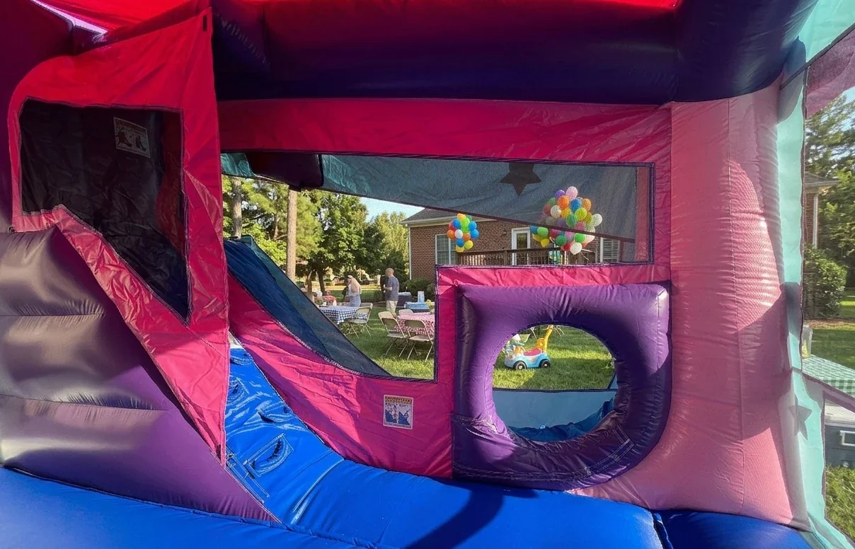 Interior view of the Magical Unicorn Bounce House rental showing the internal slide, crawl-through obstacle, and safety mesh windows at a party in Holly Springs.